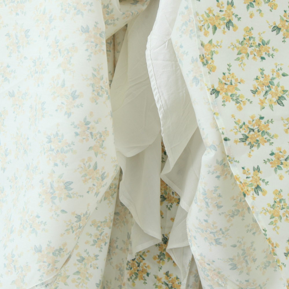 Bloemenprint stof met gele en blauwe bloemen op witte achtergrond, gedrapeerd en gelaagd. Perfect voor interieurdecoratie en modeontwerp.
