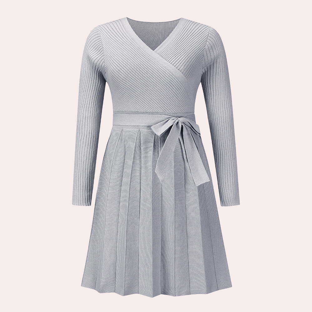 Grijze gebreide damesjurk met lange mouwen, V-hals en strikceintuur. Elegante plissérok, ideaal voor herfstmode. Comfortabele en stijlvolle outfit.