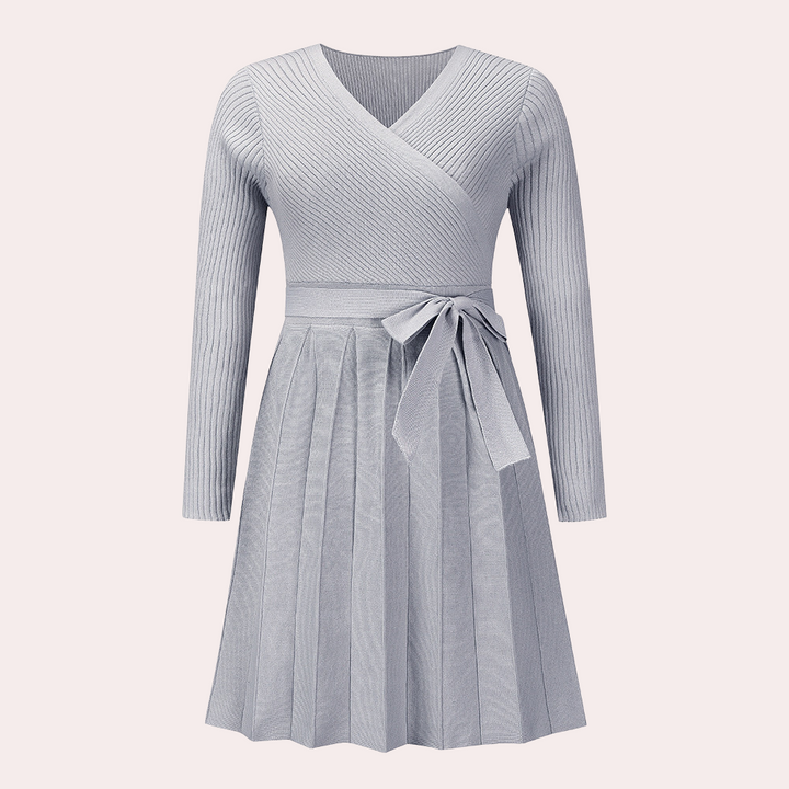 Grijze gebreide damesjurk met lange mouwen, V-hals en strikceintuur. Elegante plissérok, ideaal voor herfstmode. Comfortabele en stijlvolle outfit.