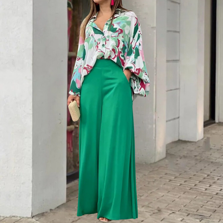 Vrouw in groene wijde broek en kleurrijke blouse, staand op stoep. Stijlvolle mode, zomerse outfit, trendy kleding, stedelijke achtergrond.