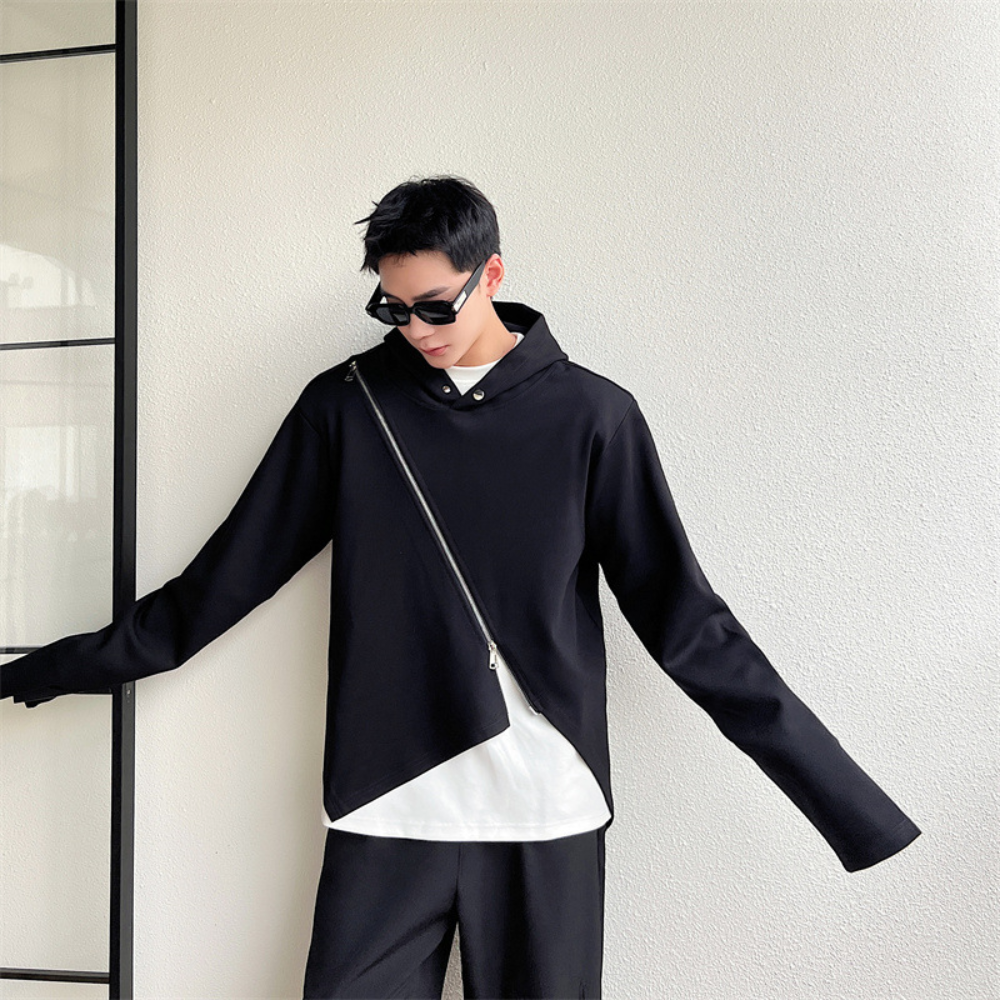 Zwarte asymmetrische jas met schuine rits, gedragen door een persoon met zonnebril. Moderne mode, minimalistisch design, trendy herenkleding.