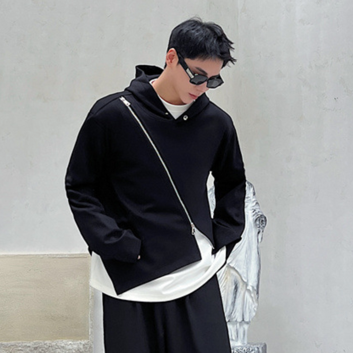 Zwarte asymmetrische hoodie met diagonale rits, gedragen door man met zonnebril. Moderne streetwear, minimalistisch design, casual mode.