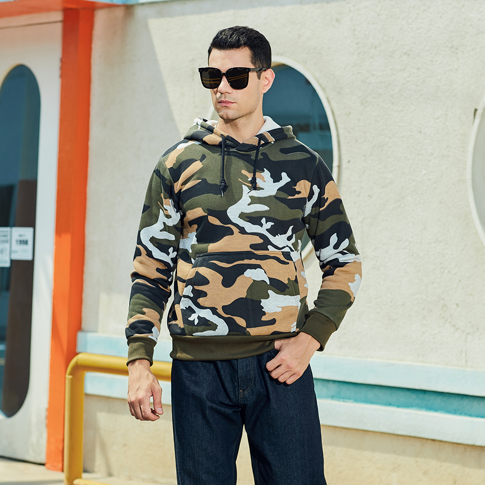 Man in camouflage hoodie en zonnebril, buiten voor modern gebouw. Stijlvolle herenkleding, casual mode, urban streetwear.