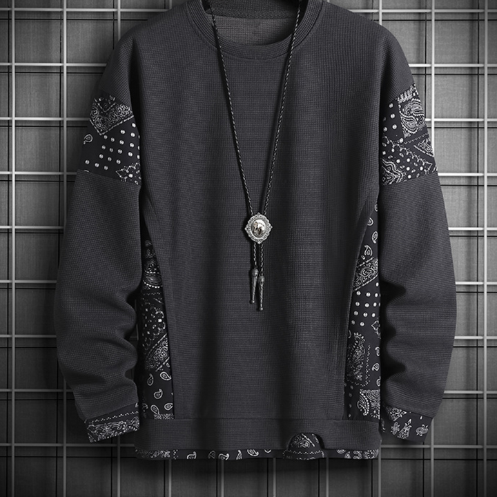Donkergrijze trui met paisley-patronen op mouwen, hangend aan een rasterachtergrond. Modieuze herenkleding, casual stijl, trendy ontwerp.