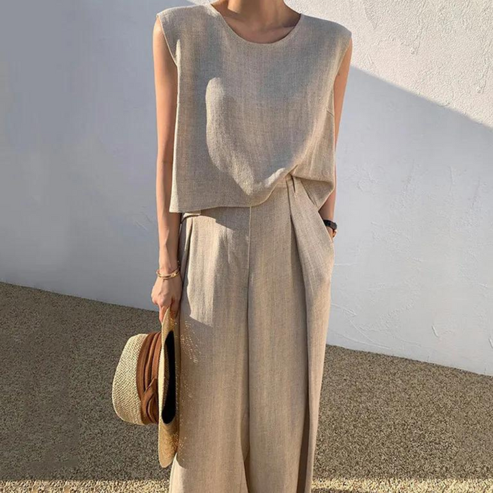 Vrouw in beige linnen outfit met mouwloos topje en wijde broek, houdt strohoed vast. Zomermode, casual chique stijl, minimalistisch design.