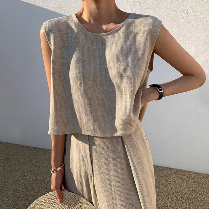 Vrouw in beige mouwloze top en broek, minimalistische zomermode, casual chique stijl, buiten gefotografeerd tegen witte muur.