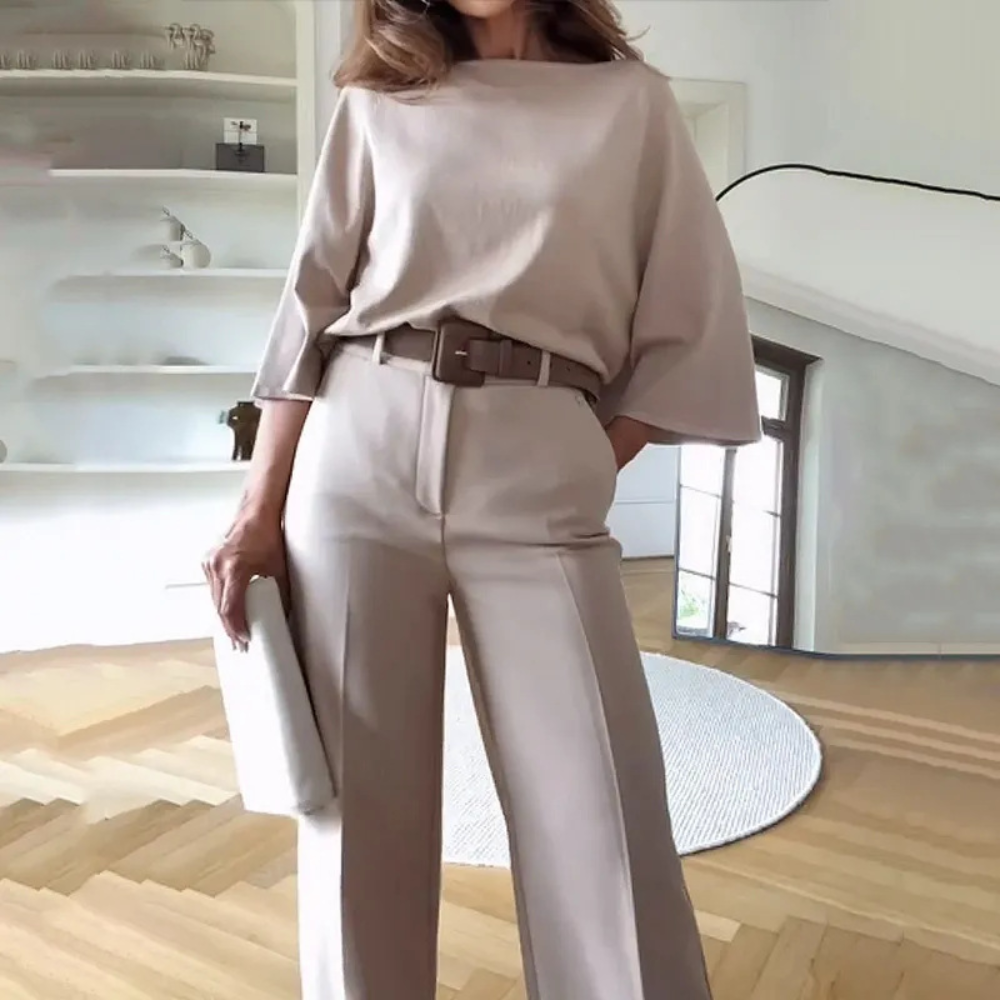 Vrouw in stijlvolle beige outfit met wijde broek en riem, staand in moderne woonkamer. Mode, minimalistisch design, interieur.