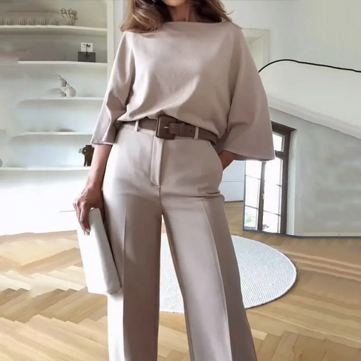 Vrouw in stijlvolle beige outfit met wijde broek en riem, staand in moderne woonkamer. Mode, minimalistisch design, interieur.