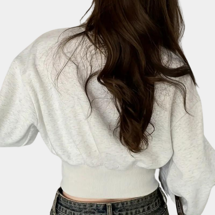 Vrouw in witte cropped trui met lange mouwen en golvend bruin haar, gezien van achteren. Casual mode, trendy dameskleding, herfststijl.