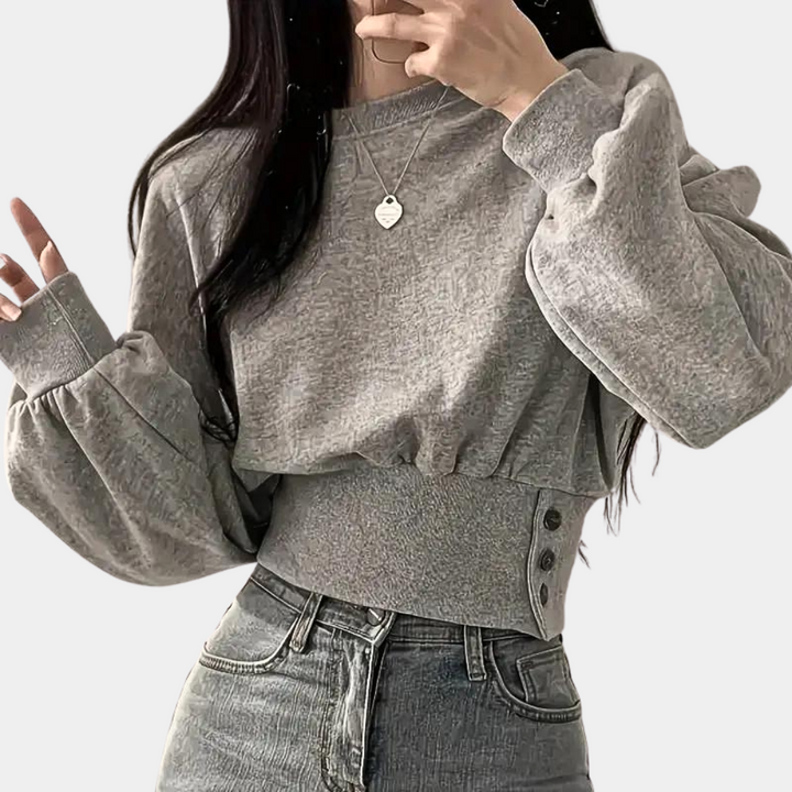 Grijze cropped trui met ballonmouwen en knoopdetails, gedragen door vrouw. Modieuze dameskleding, casual stijl, comfortabele pasvorm.