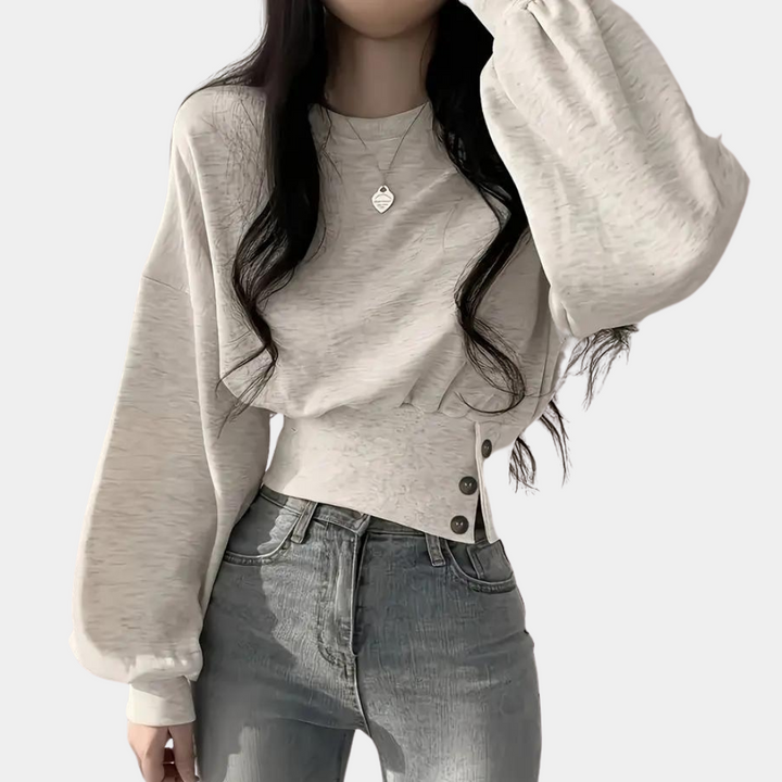 Lichtgrijze trui met ballonmouwen en knoopdetails, gedragen door een vrouw. Modieuze dameskleding, casual stijl, trendy outfit.