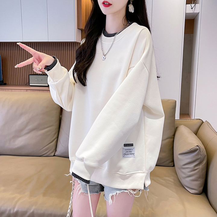 Vrouw in oversized crèmekleurige trui met grijze shorts, poseert in moderne woonkamer. Trendy casual outfit, comfortabele mode, herfststijl.