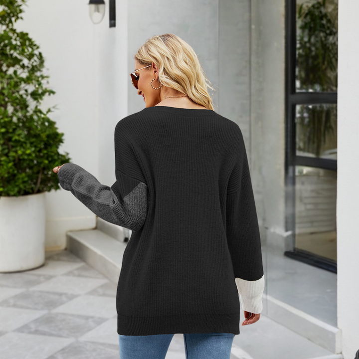 Vrouw in zwarte trui met grijze en witte mouwen, draagt zonnebril, staat buiten bij moderne architectuur. Casual mode, herfstkleding.