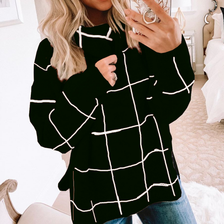 Vrouw in zwarte trui met wit ruitpatroon, casual mode, selfie in slaapkamer, trendy dameskleding, herfst-winter outfit, comfortabele stijl.