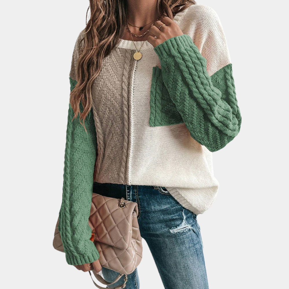 Vrouw draagt gebreide trui met groene en beige kleurblokken, gecombineerd met spijkerbroek en beige handtas. Modieuze dameskleding herfst.