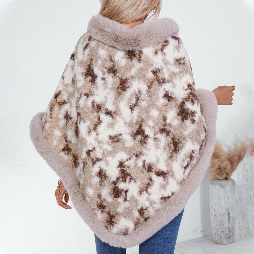 Vrouw draagt stijlvolle, warme poncho met beige en bruine camouflageprint, afgewerkt met zachte, pluizige rand. Perfect voor herfstmode en winterstijl.