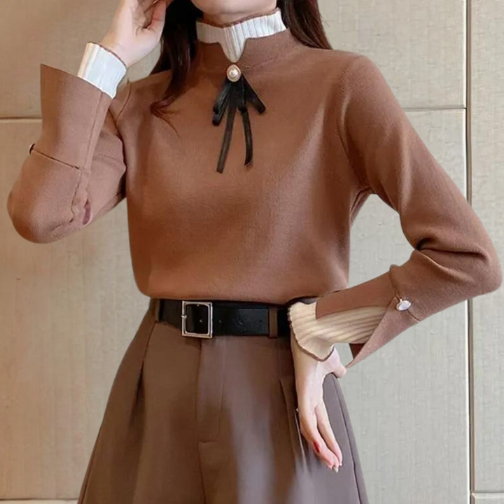 Vrouw in bruine trui met zwarte strik en parel, hoge kraag, gecombineerd met bruine broek en zwarte riem. Elegante herfstmode, dameskleding.