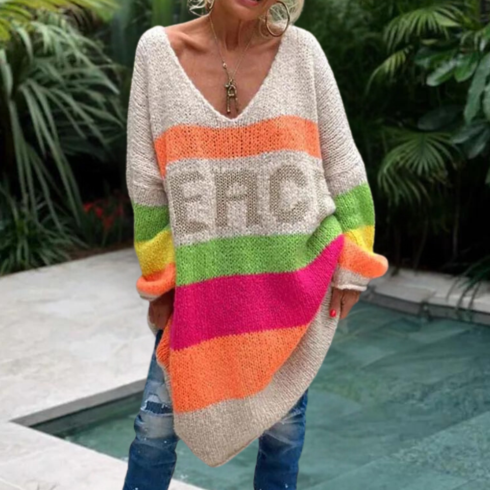 Vrouw in oversized trui met kleurrijke strepen en "PEACE" tekst, bij zwembad. Trendy mode, casual stijl, comfortabele kleding.