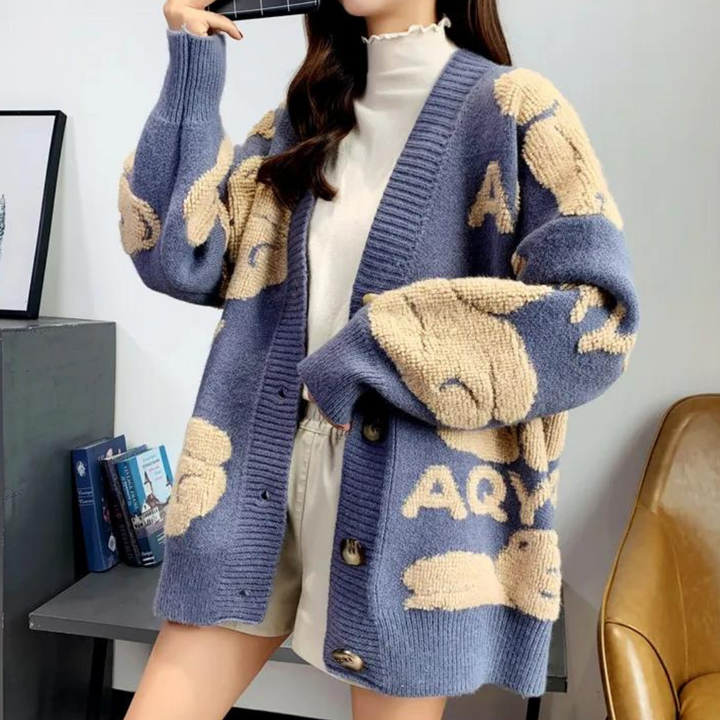 Vrouw draagt blauwe oversized cardigan met beige konijnenprint en knopen, gecombineerd met witte top en korte broek. Trendy damesmode, herfststijl.