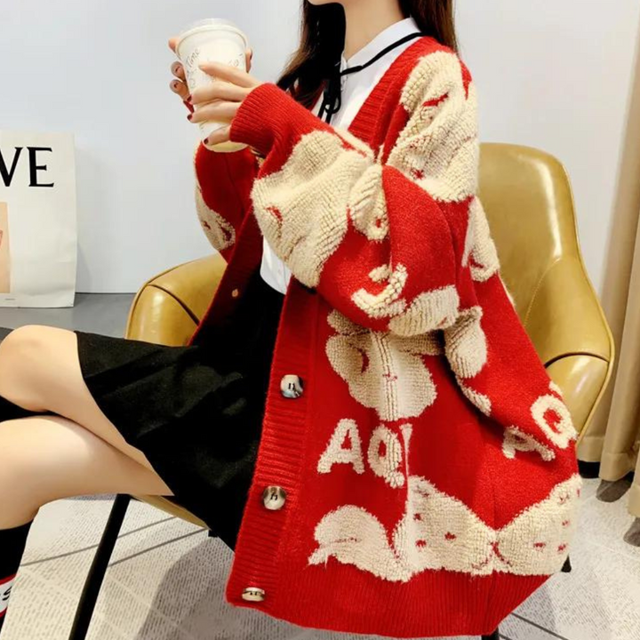 Vrouw in rode gebreide trui met witte patronen, zittend op een stoel, drinkt koffie. Modieuze dameskleding, herfststijl, comfortabele outfit.