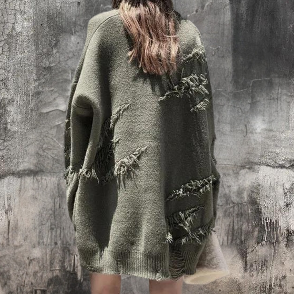 Groene oversized trui met rafelige details, gedragen door een persoon tegen een betonnen muur. Modieuze, casual herfstkleding voor dames.
