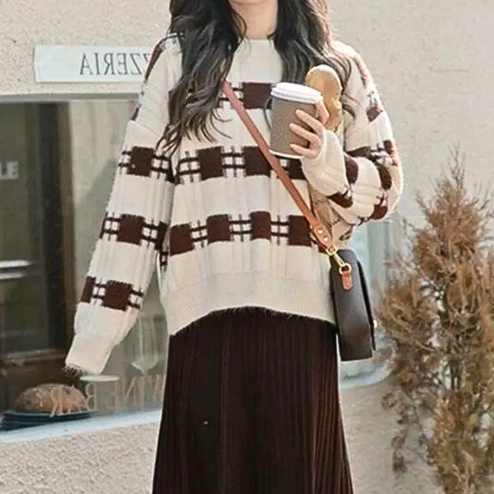 Vrouw in gebreide trui met ruitpatroon, bruine rok en schoudertas, houdt een koffiebeker vast. Stijlvolle herfstmode, casual outfit.
