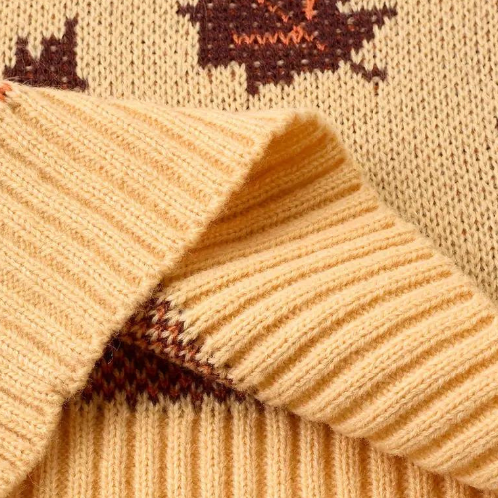 Beige gebreide trui met bruine herfstbladeren, close-up van zachte stof en ribgebreide manchetten. Perfect voor herfstmode en warme kleding.