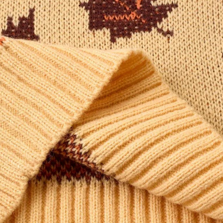 Beige gebreide trui met bruine herfstbladeren, close-up van zachte stof en ribgebreide manchetten. Perfect voor herfstmode en warme kleding.