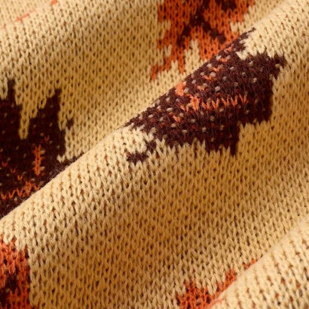 Beige gebreide stof met herfstbladeren patroon in bruin en oranje, close-up textuur. Perfect voor herfstmode en interieurdecoratie.