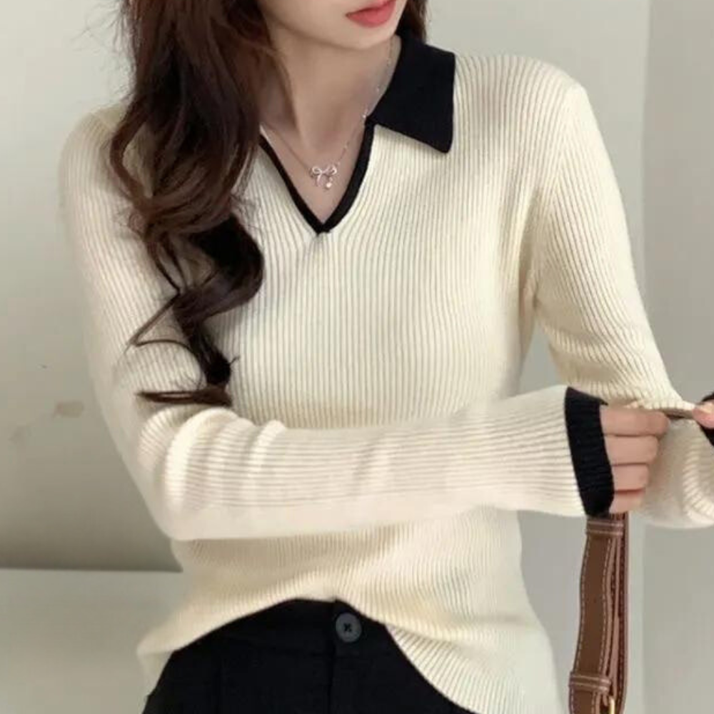 Vrouw in crèmekleurige trui met zwarte kraag en manchetten, draagt een bruine tas. Modieuze dameskleding, herfststijl, casual chic.