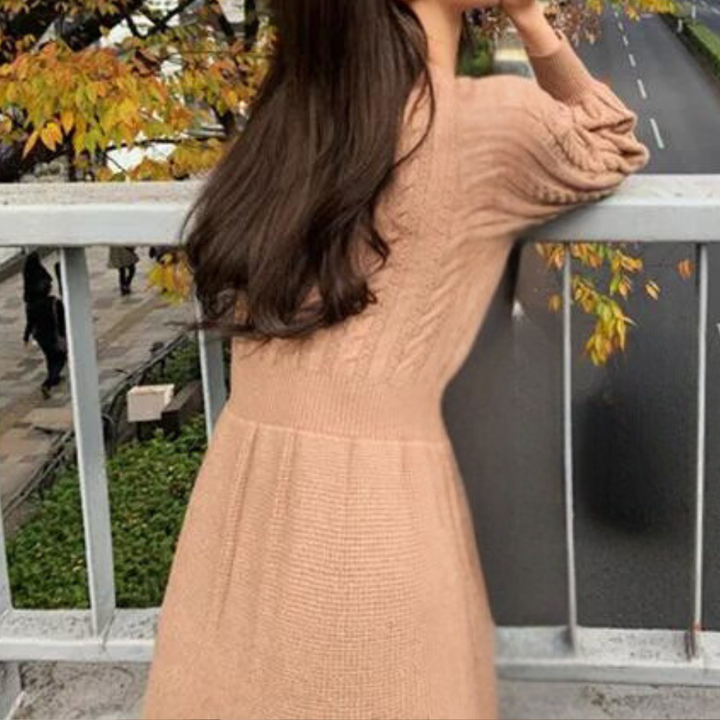 Vrouw in beige gebreide jurk leunt op brugleuning, herfstbladeren op achtergrond. Modieuze herfstkleding, casual damesmode, buitenfotografie.