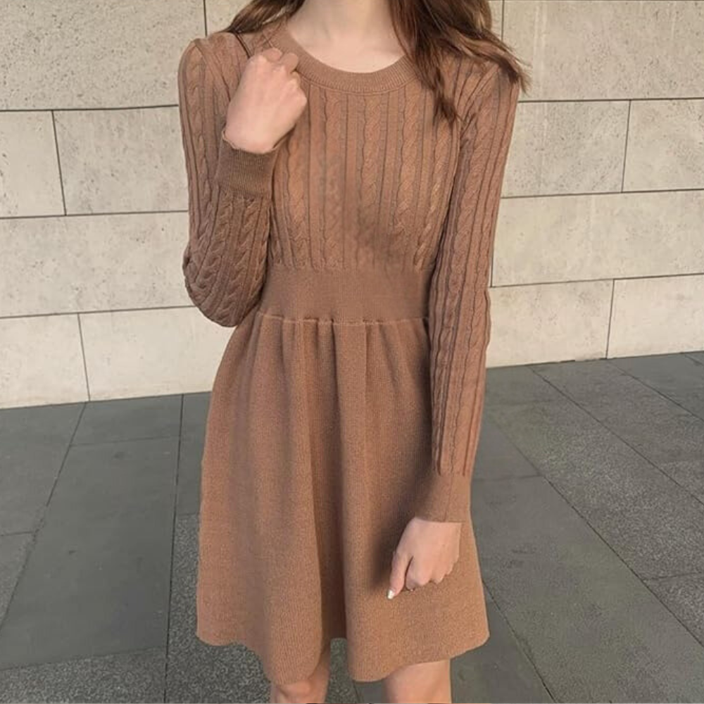 Vrouw in elegante, gebreide bruine jurk met lange mouwen, staand tegen een stenen muur. Modieuze dameskleding, herfststijl, casual chic.