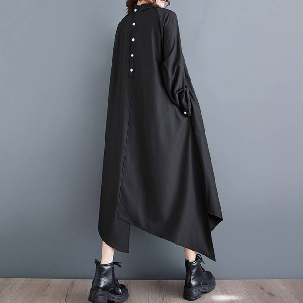 Zwarte asymmetrische jurk met knopen op de rug, gedragen door een persoon, gecombineerd met zwarte laarzen. Modieuze dameskleding, minimalistisch design.