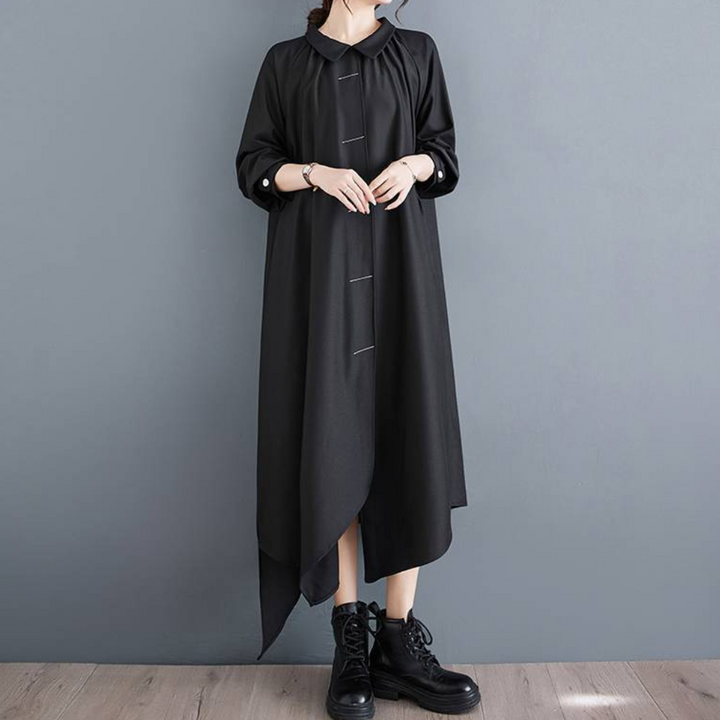 Zwarte asymmetrische jurk met lange mouwen en knoopsluiting, gedragen door een model met zwarte laarzen. Elegante damesmode, minimalistisch ontwerp.
