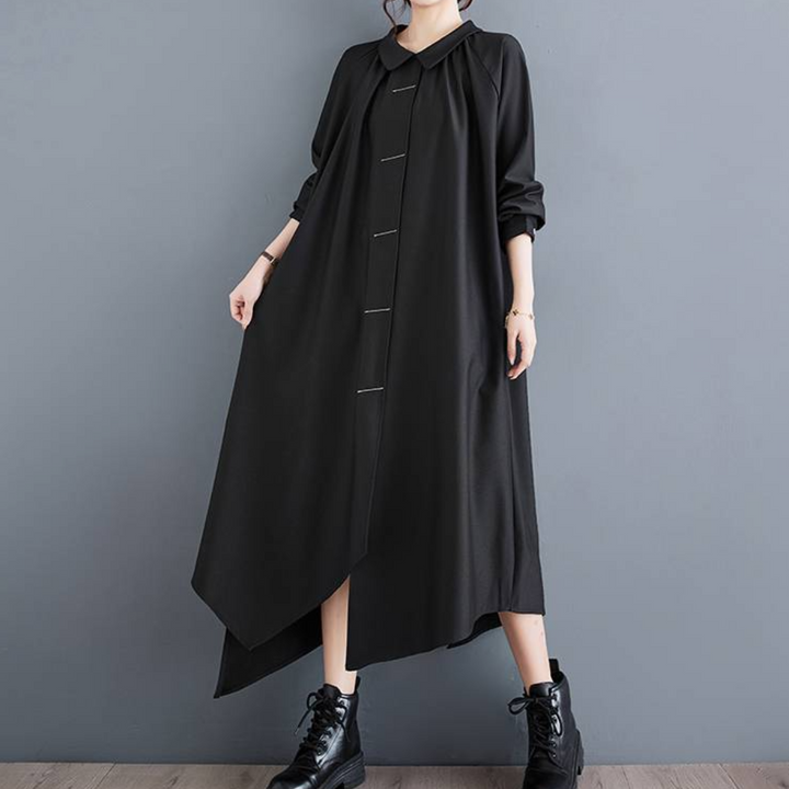 Zwarte asymmetrische maxi-jurk met lange mouwen en knoopsluiting, gedragen door model met zwarte veterlaarzen. Elegante damesmode.