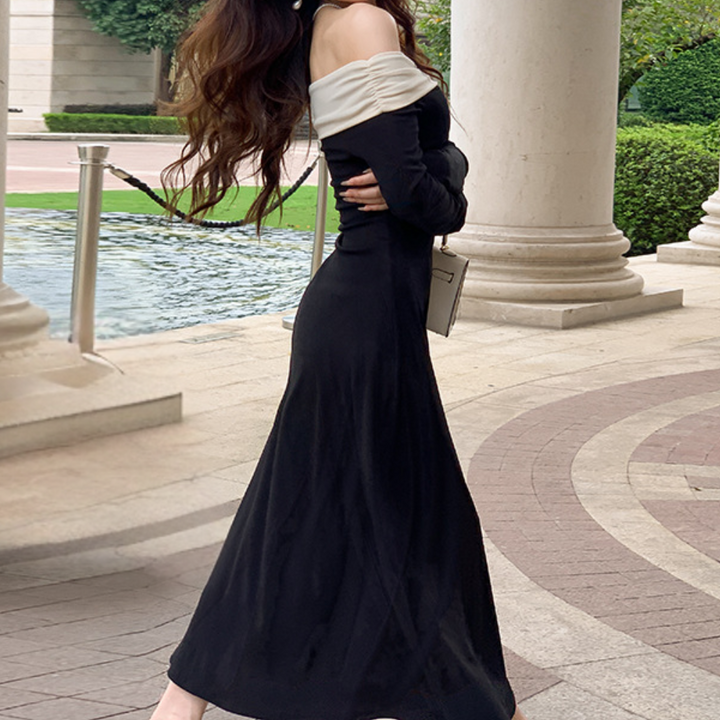 Vrouw in elegante zwarte avondjurk met witte off-shoulder details, staand bij een klassieke zuilengang. Luxe mode, stijlvolle avondkleding.