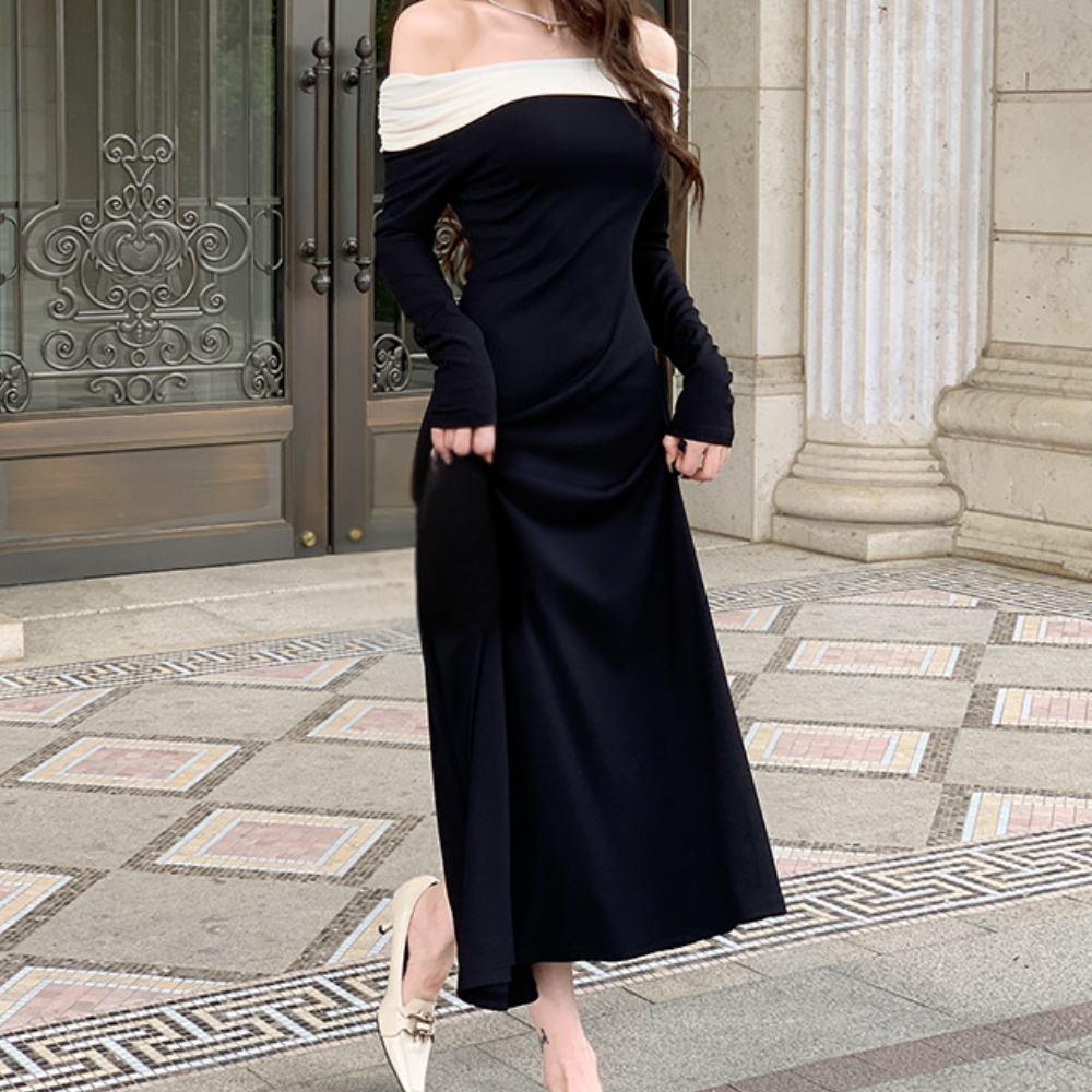 Vrouw in elegante zwarte off-shoulder jurk met lange mouwen, staand voor een sierlijke deur. Stijlvolle mode, avondkleding, chique uitstraling.