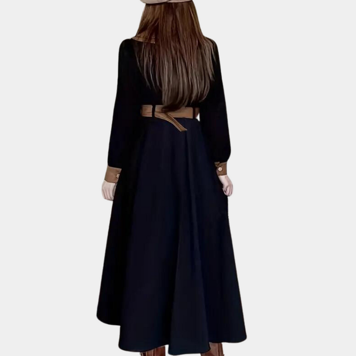 Vrouw in lange zwarte jurk met bruine riem en hoed, gezien van achteren. Elegante mode, herfstkleding, stijlvolle damesoutfit.