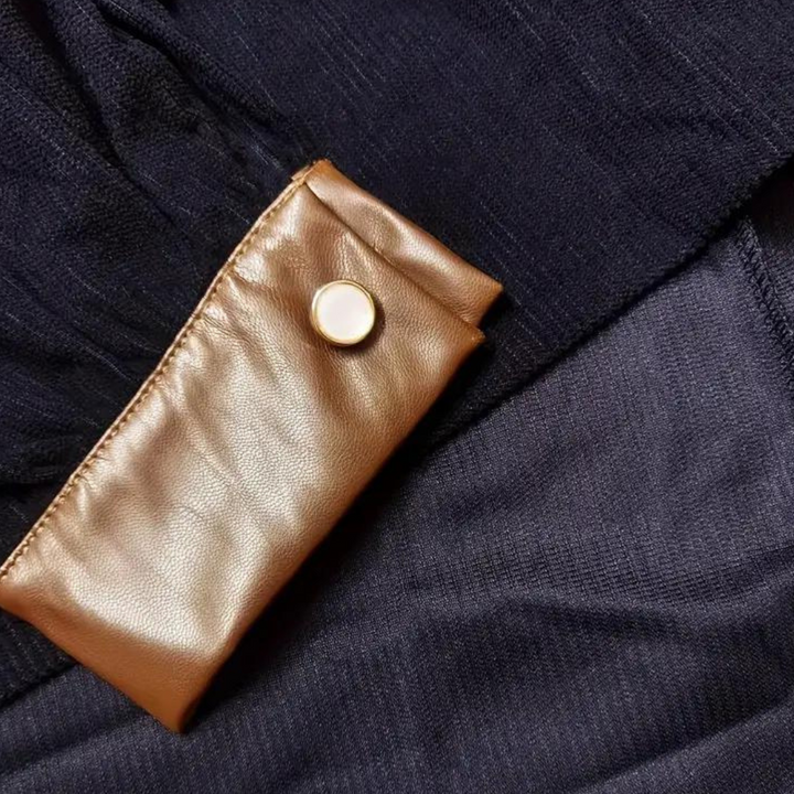 Donkerblauwe stof met gouden knoop en glanzende leren details. Luxe textiel, elegante afwerking, hoogwaardige materialen. Perfect voor modeontwerp.