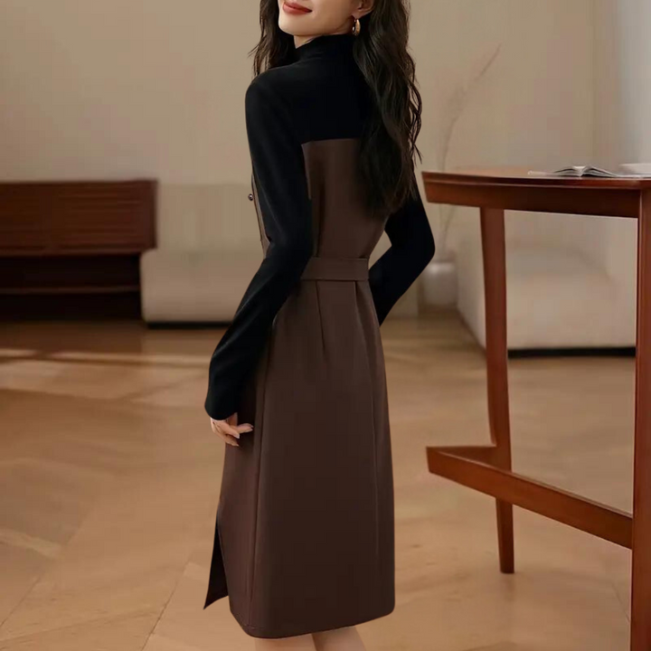 Vrouw in stijlvolle bruine en zwarte jurk met lange mouwen, staand in moderne woonkamer. Elegante mode, herfstkleding, minimalistisch interieur.
