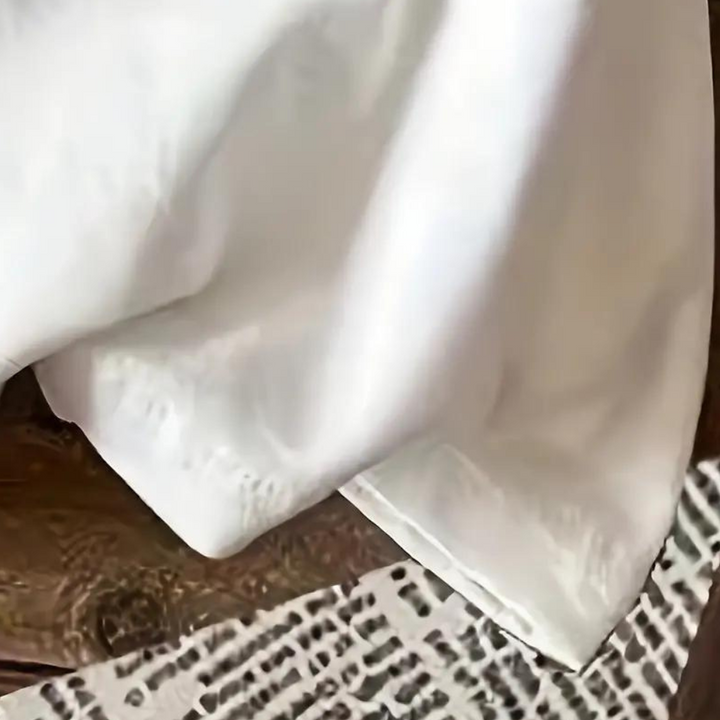 Witte satijnen blouse op houten tafel, elegant en stijlvol, perfect voor formele gelegenheden. Luxe damesmode, hoogwaardige stof.