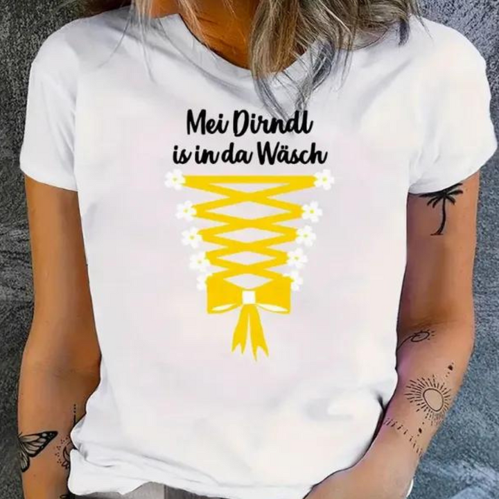 Witte T-shirt met gele dirndl-print en tekst "Mei Dirndl is in da Wäsch", gedragen door vrouw. Perfect voor Oktoberfest, casual mode.