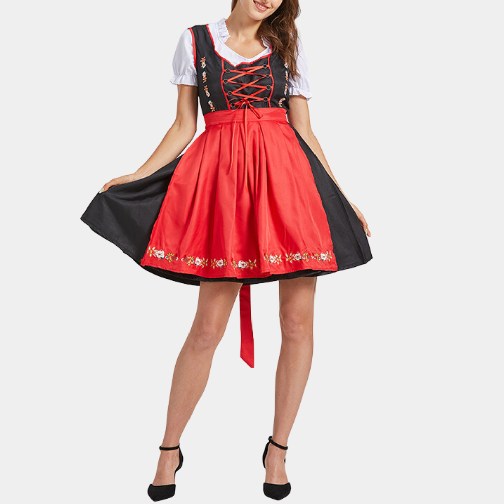 Vrouw in traditionele Duitse dirndl jurk met rood schort en geborduurde details, perfect voor Oktoberfest. Elegante zwarte hakken completeren de look.