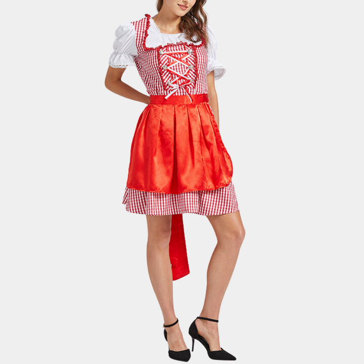 Vrouw in rood-wit geblokte dirndl jurk met schort, traditionele Beierse kleding, Oktoberfest outfit, witte blouse, zwarte hakken.