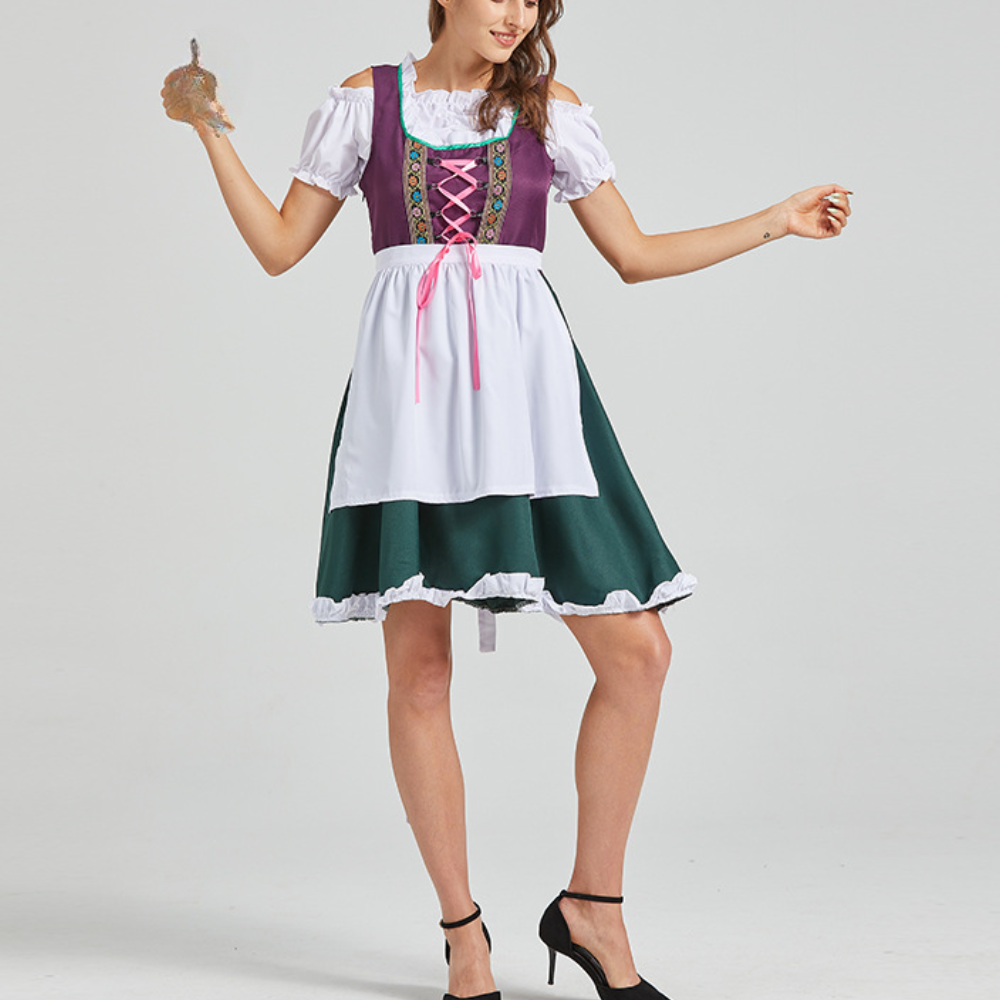 Vrouw in traditionele Duitse dirndl jurk met paarse top, witte schort en groene rok, poseert met pretzel. Oktoberfest kleding.