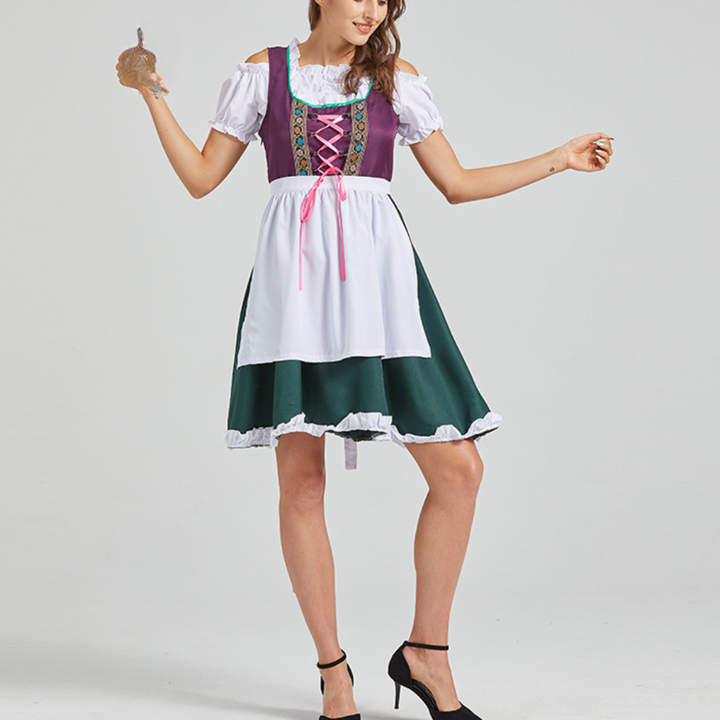 Vrouw in traditionele Duitse dirndl jurk met paarse top, witte schort en groene rok, poseert met pretzel. Oktoberfest kleding.