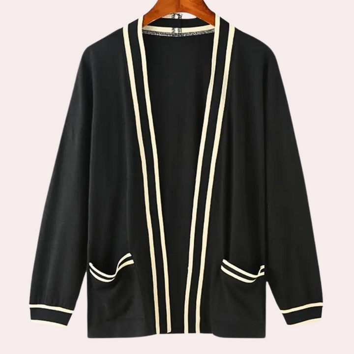 Zwarte cardigan met witte strepen, open voorkant en zakken, hangend aan een houten hanger. Stijlvolle dameskleding, casual en elegant ontwerp.