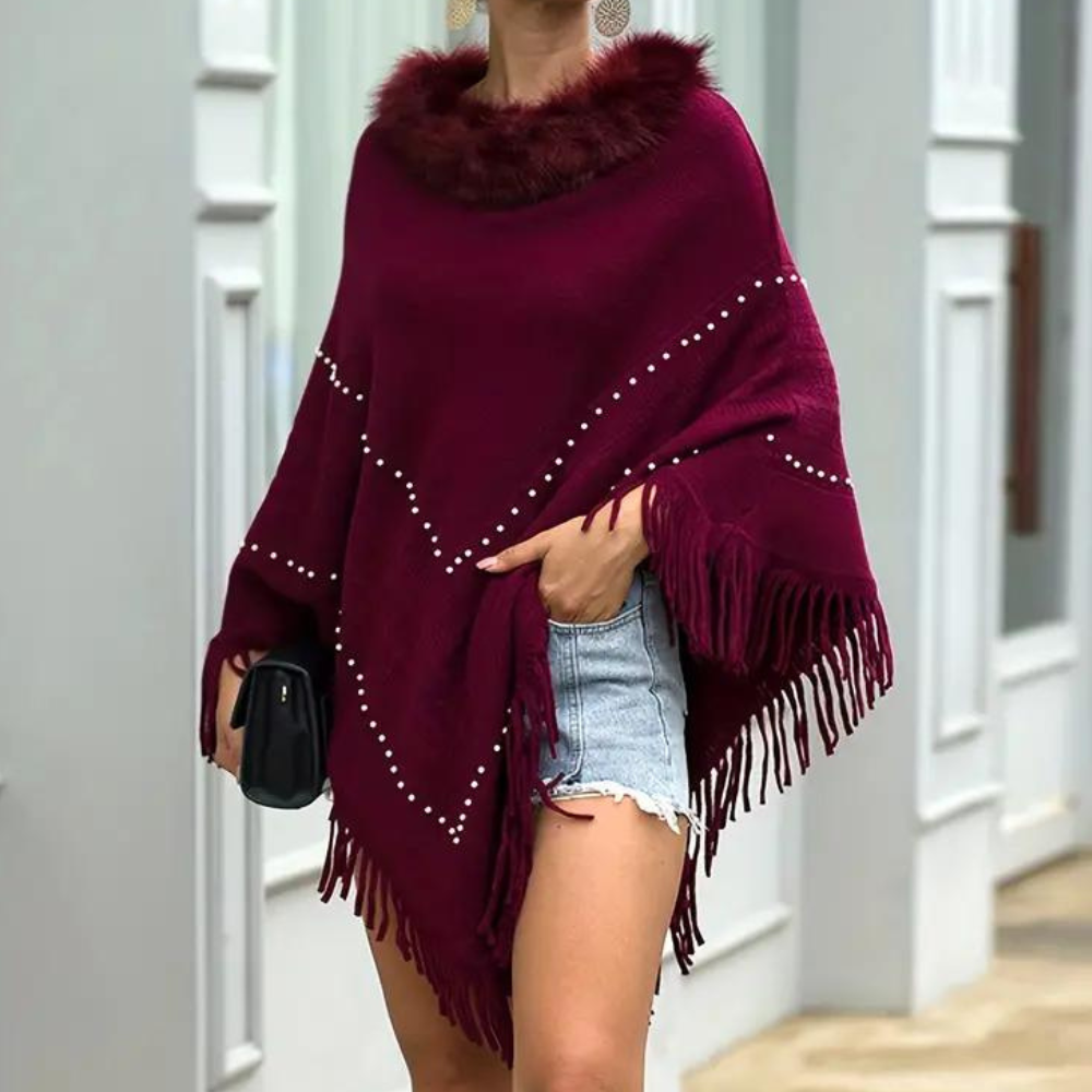 Vrouw draagt bordeauxrode poncho met franjes en pareldetails, gecombineerd met spijkershorts. Modieuze herfstoutfit, stijlvolle dameskleding.