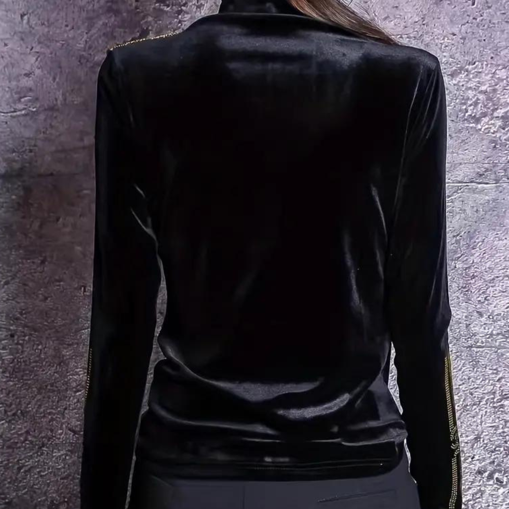 Zwarte fluwelen dames top met lange mouwen en gouden ritsdetails, gezien van achteren tegen een grijze achtergrond. Elegante en stijlvolle kleding.