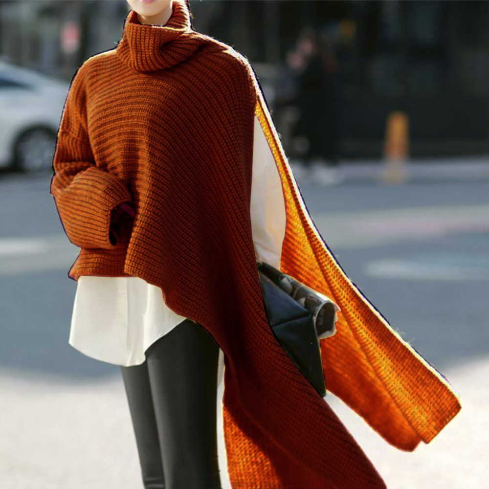 Vrouw draagt een stijlvolle, baksteenrode poncho met coltrui, gecombineerd met een witte blouse en zwarte broek. Perfect voor herfstmode.